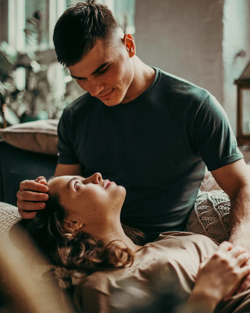 Man looking with love at woman while she lays with her head on his legs.