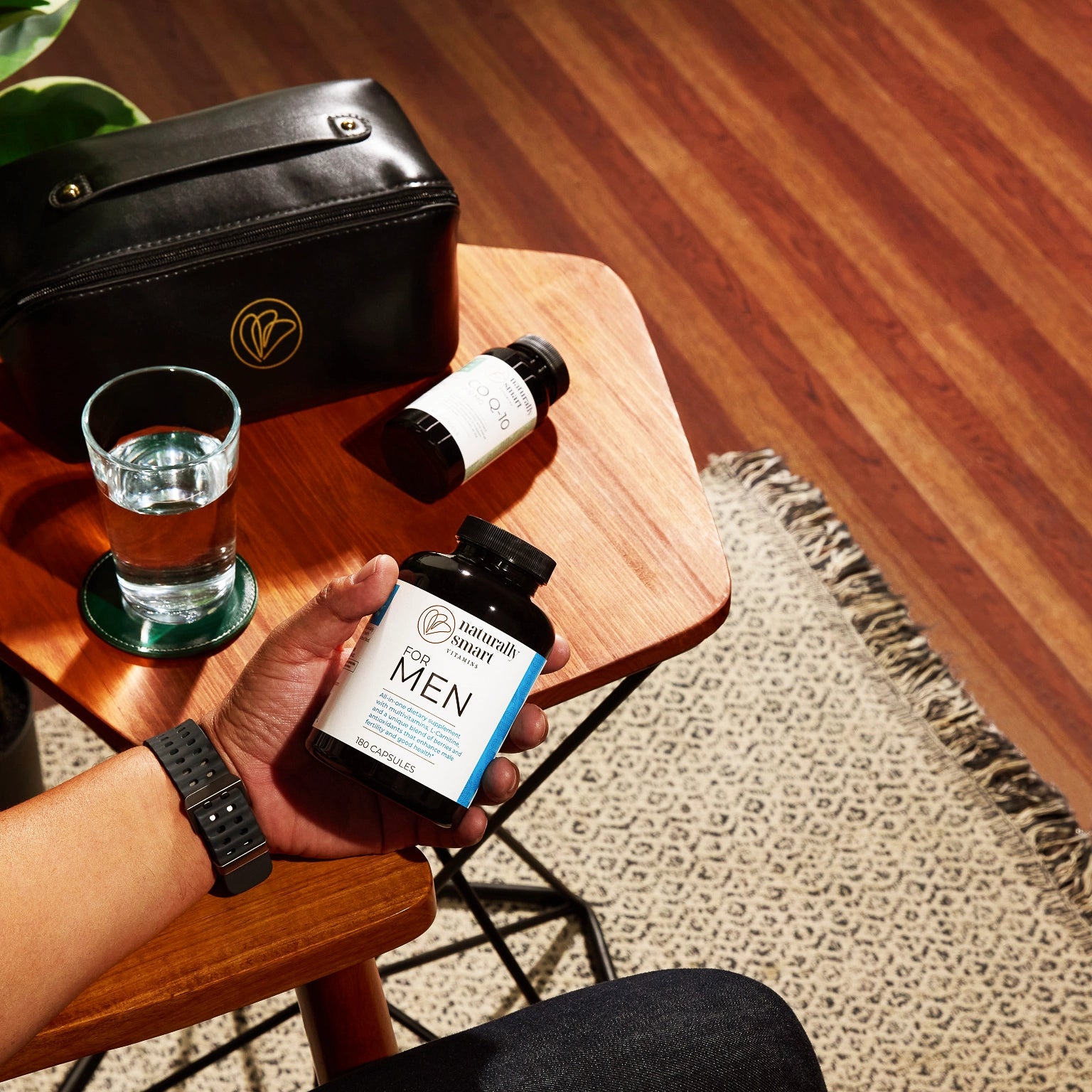 man holding bottle of naturally smart for men bottle with a glass of water next to him.